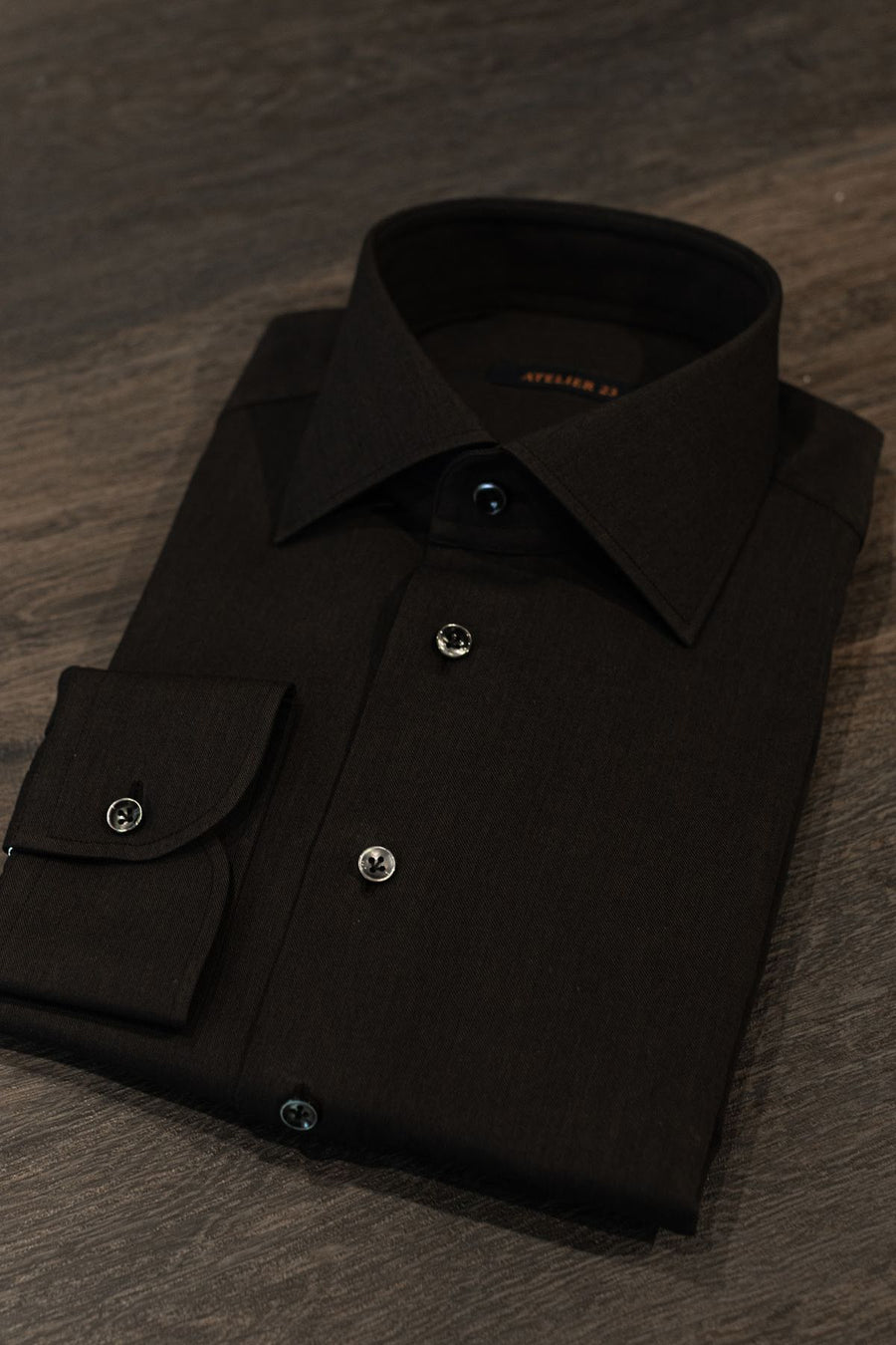 Camisa preta ATELIER 23 dobrada sobre uma mesa escura