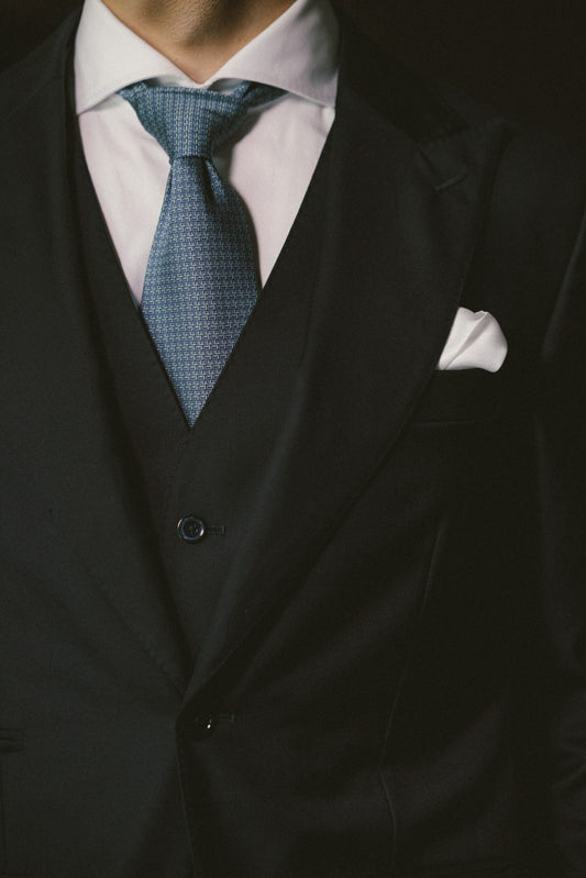 Dark three-piece ATELIER 23 suit with a blue silk tie and a white pocket square