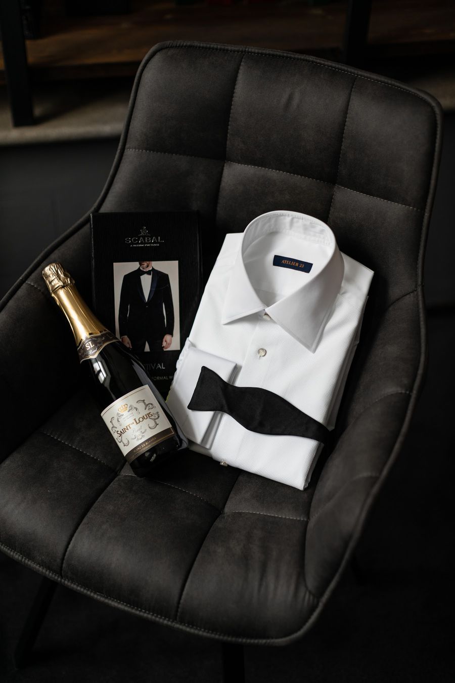 Camisa branca, laço preto e champanhe numa poltrona