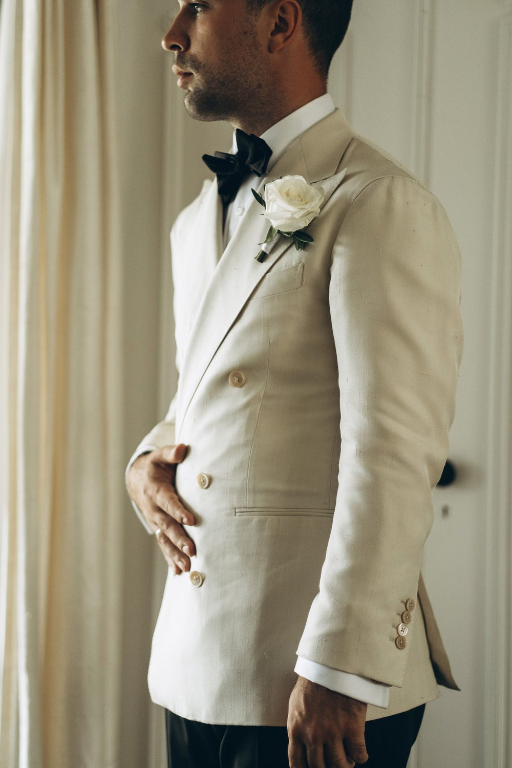 Groom in an ivory double-breasted dinner jacket with a white rose